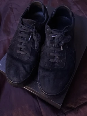 Svarta låga sneakers från Axel Arigato - Snygga svarta sneakers i mocka med klassisk låg profil och svarta skosnören. Skorna har en stilren design med ton-i-ton detaljer och rundad tå. Perfekta för dig som gillar en clean och enkel look till vardagsoutfiten. Skorna har blivit ganska låga på sulorna, men påverkar inte skornas funktion. Därför säljs den billigt, pris kan diskuteras