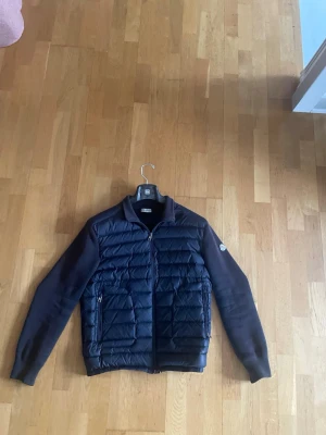 Mörkblå cardigan från Moncler - Snygg mörkblå cardigan från Moncler med quiltad front och ärmar i stickad bomull. Jackan har dragkedja framtill, två sidofickor med dragkedja och en klassisk Moncler-logga på ärmen. Perfekt för kalla vinterdagar och riktigt stilren look. Äkta såklart, storlek L men passar M bättre. Pris är diskuterbart. 