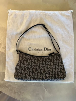 Christian Dior monogram axelremsväska - Christian Dior axelremsväska från 2002 med klassiskt monogrammönster i marinblått, svart och grått med justerbart band. Original dustbag och äkthetsintyg medföljer. Väskan är i använt skick med slitage och mindre skador på hörn samt vid remfästen (se bilder, fler bilder finns vid efterfrågan). Insidan är i fint skick. 💘