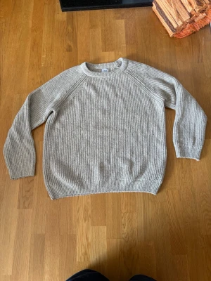 Ljusbiege stickad tröja i ullmix - Mysig ljusgrå stickad tröja med rund hals och raglanärmar. Tröjan har ribbstickad struktur och är tillverkad i en mjuk ullblandning. Perfekt för lager-på-lager och passar till både jeans och kjol.
