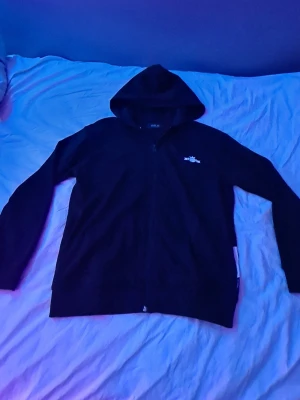 Svart hoodie från Replay - Säljer en svart hoodie från Replay med dragkedja framtill och liten logga på bröstet. Hoodien har huva och långa ärmar, perfekt för en chill och avslappnad stil. Materialet känns mjukt och bekvämt, passar till det mesta i garderoben.