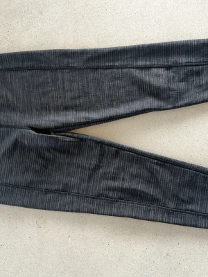 Mörkgrå leggings från High Mountain - Snygga mörkgrå leggings från High Mountain med diskret melerad look och bred resår i midjan med logga. Tillverkade i stretchigt och mjukt material som sitter skönt på kroppen. Perfekta för en aktiv vardag eller chill hemma.