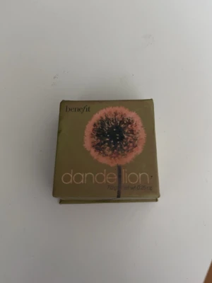 Benefit Dandelion rouge - Säljer ett Benefit Dandelion rouge i en söt fyrkantig kartongförpackning. Rouget har en ljusrosa nyans som ger en fräsch och naturlig look. Perfekt för att ge kinderna en mjuk och subtil färg. Kommer i en kompakt dosa med spegel.