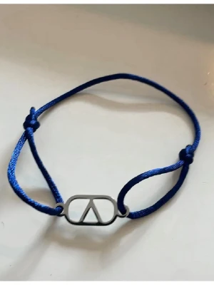 Blått armband med silver detalj - Snyggt armband med marinblått justerbart band och en silverfärgad metallbricka. Perfekt accessoar för att lyfta din stil med en touch av lyx och enkelhet. Passar till många olika outfits och är lätt att bära varje dag.