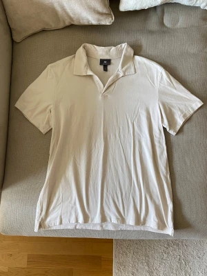Beige pikétröja från H&M - Snygg beige pikétröja från H&M i regular fit. Tröjan har klassisk krage och korta ärmar, perfekt för en avslappnad men stilren look. Tillverkad i mjukt bomullsmaterial som känns skönt mot huden.