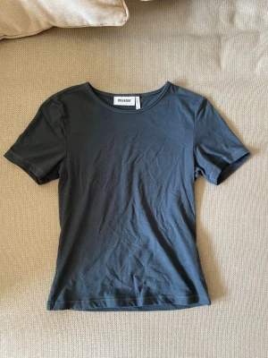 Mörkgrå t-shirt från Weekday - En stilren mörkgrå t-shirt från Weekday i mjuk bomull. Klassisk rund halsringning och korta ärmar. Perfekt basplagg att matcha med allt i garderoben.