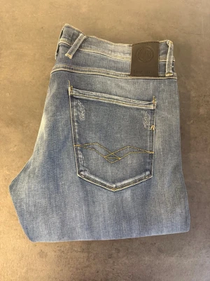 Ljusblå slim fit jeans från Replay stl 33/32 - Snygga ljusblå jeans från Replay med slim fit passform. Jeansen har klassisk femficksdesign, broderad bakficka och diskreta slitningar. Perfekta för en avslappnad och trendig look. Materialet är mjukt denim med stretch för extra komfort.