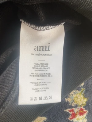 Ami Paris - Snygg svart hoodie från Ami Paris med klassisk design och ribbade muddar. Tillverkad i Portugal och har en mjuk bomullskänsla. Perfekt för dig som gillar stilrena plagg med diskret logga i nacken.