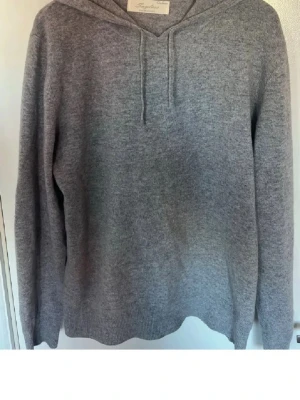 Grå hoodie från Soft Goat - Mjuk och stilren grå hoodie från sayless i kashmirblandning. Tröjan har huva med dragsko och långa ärmar. Perfekt för dig som gillar en enkel och clean look. Ribbstickad nederkant och ärmslut ger en snygg passform.
