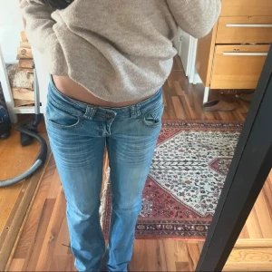 Lågmidjade ljusblå jeans från Sky Rebel - Säljer ett par riktigt snygga lågmidjade jeans från Sky Rebel i ljusblå tvätt. Jeansen har coola detaljer vid fickorna och unika knappar framtill. Materialet är klassisk denim med kontrastsömmar och broderad etikett på insidan.
