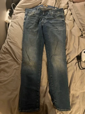 Blå jeans från Jack & Jones - Säljer ett par klassiska blå jeans från Jack & Jones i modellen Glenn. Jeansen har en slim fit-passform, fem fickor och snygga slitningar på låren. Tillverkade i denim med en skön stretch för extra komfort.