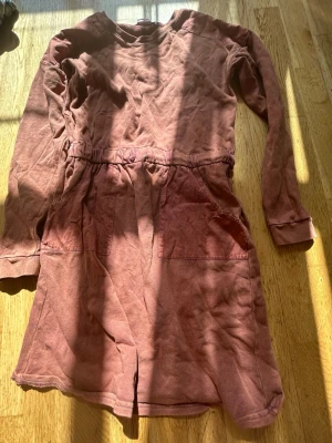 Rostbrun jumpsuit från H&M - En mjuk och skön rostbrun jumpsuit från H&M med långa ärmar och resår i midjan. Jumpsuiten har två stora fickor framtill och är tillverkad i bomull. Perfekt för en avslappnad och trendig look.