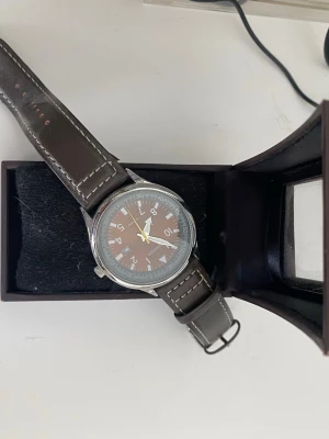 Brun analog klocka från Weshine - Stilren klocka från Weshine med brun urtavla och tydliga vita siffror. Klockan har ett klassiskt brunt läderarmband med ljusa sömmar och silverfärgat boett. Perfekt accessoar för en snygg och tidlös look.