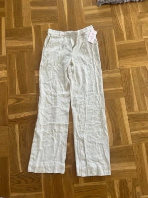 Beige linnebyxor med raka ben - Säljer ett par beige linnebyxor med raka ben och hög midja. Byxorna har resår i midjan baktill och sidofickor. Perfekta för en avslappnad och stilren look. Materialet är luftigt linne som ger en skön känsla. Köpte de för 499kr.