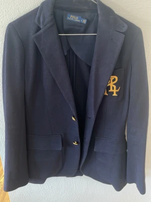 Polo Ralph Lauren marinblå corduroy kavaj – storlek 4 (160/88A) - Säljer fin Polo Ralph Lauren kavaj i marinblå corduroy i storlek 4 (XS/S, 160/88A). Klassisk modell med guldknappar och broderat logo på bröstfickan. Bra kvalitet och fint skick! ✨ Perfekt till jeans eller kjol – både vardag och fest. Varm höst/vinterkavaj. Nypris runt 2000+ kr. Frågor? Skriv gärna! Kan skickas snabbt 😊