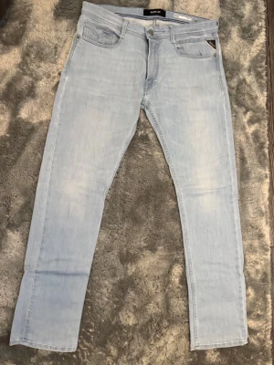 Ljusblå jeans från Replay Rocco Storlek 32 - Snygga ljusblå jeans från Replay, modell Rocco Comfort Fit. Klassisk femficksdesign med Replay-logga på myntfickan och knappgylf. Jeansen har raka ben och är tillverkade i mjukt denimtyg som ger en avslappnad look. Storlek 32