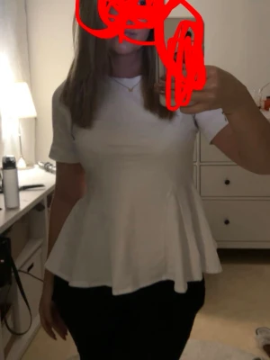 Vit topp  - Snygg vit peplum topp med korta ärmar och rund hals. Toppen har en figurnära passform upptill och ett utställd volang nedtill som ger en feminin siluett. Perfekt att styla med jeans eller kjol för en trendig look.