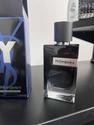 Yves Saint Laurent Y Eau de Parfum - Y Eau de Parfum från Yves Saint Laurent är en stilren parfym i en mörkblå glasflaska med silverdetaljer och en robust, texturerad kork. Flaskan har en modern, fyrkantig form och rymmer 100 ml. Perfekt för dig som gillar exklusiva och eleganta dofter.