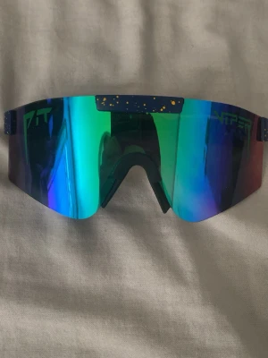 Blå-gröna Pit Viper solglasögon - Säljer ett par riktigt feta Pit Viper solglasögon med spegelblå och gröna linser. Modellen har en sportig, futuristisk skärmform och blå båge med gula stänk. Perfekta för dig som vill sticka ut och skydda ögonen mot solen. Den är i bra skick och knappast använd💪orginal påse kommer med💪pris kan diskuteras!