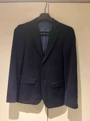 Mörkblå kostym Dressman slimfit - Mörkblå kostym från Dressman i mycket bra skick, bara använd 2gånger.                                              Byxor storlek: 27:30                                                        Kavaj storlek: 42 (short) slimfit.                                         Inga defekter.                                                                     Allt medföljer i köpet:) dvs byxor och kavaj.                Båda är samma serige och båda är slimfit.              Vid frågor är det bara att skriva:)