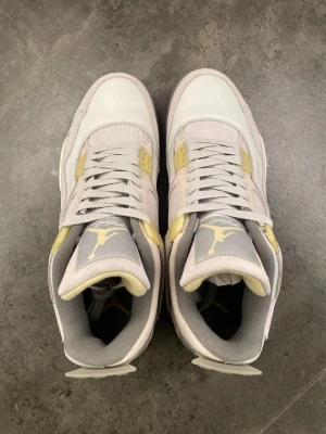 Jordan 4 Retro Off White och Gul - Säljer ett par Jordan 4 Retro sneakers i off white och ljusgul med grå detaljer. Skorna har meshpaneler, klassiska snörningar och Jumpman-logga på plösen. Ovandelen är i en mix av läder och textil, vilket ger en schysst och sportig look.