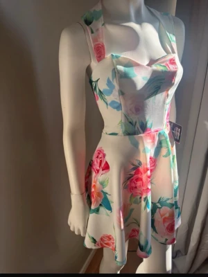Vit blommig sommarklänning strl S  - Supersöt vit klänning med färgglatt blommönster  Klänningen har breda axelband, hjärtformad urringning och en utställd kjol som ger en lekfull look. Perfekt för varma dagar och har en fräsch, ungdomlig vibe. Ingen prislapp kvar i men helt ny och aldrig använd