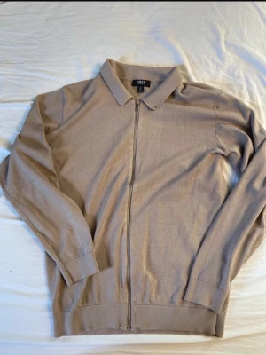 Beige ziptröja med krage från H&M - Stilren beige ziptröja från H&M med klassisk krage och hel dragkedja framtill. Tröjan har långa ärmar och ribbade muddar vid ärmslut och nederkant. Perfekt för en clean och enkel look.