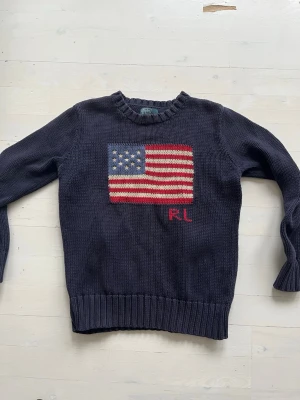 Mörkblå Ralph Lauren tröja storlek 10-12 - Mörkblå stickad tröja från Ralph Lauren med amerikansk flagga. Storlek 10-12.