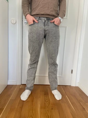 Grå tvättade raka jeans - Säljer ett par grå tvättade Woodbird jeans med rak passform och klassisk femficksdesign. Storlek 30/32 Modellen är 180cm lång
