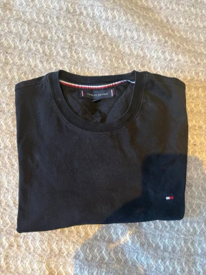 Svart Tommy Hilfiger t-shirt - Säljer en svart t-shirt från Tommy Hilfiger. Materialet är bomull och storleken är M. Tröjan är i bra skick och har inga synliga defekter.