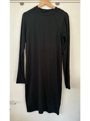 Svart långärmad Gina Tricot klänning, XL - Svart ribbad klänning från Gina Tricot i storlek XL. Långa ärmar och rund halsringning, i stretchigt halvglansigt material. Klänningen har en figurnära passform och slutar ovanför knät. En mångsidig klänning som passar för olika tillfällen. Mycket gott skick, som ny!  Skickas mot porto, kan även hämtas i Stockholm. 