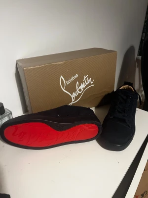 Navy sneakers från CL - Snygga mörkblåa sneakers från CL med klassisk röd sula och diskret logga. Skorna har en låg profil och är tillverkade i mocka med mörkblåa skosnören. Perfekta för dig som vill ha något exklusivt och stilrent.