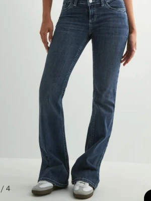 Blå bootcut jeans från Nelly - Snygga blå bootcut jeans från Nelly med klassiska kontrastsömmar och ikoniska W-detaljer på bakfickorna. Jeansen har normal midja och är tillverkade i ett mjukt denimtyg med lite stretch för extra komfort.