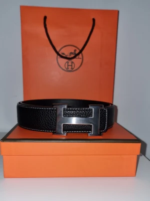 H bälte - Snyggt svart skärp från H med klassiskt H spänne i metall. Bältet är gjort i präglat skinn och levereras i original orange H box och påse. Perfekt accessoar för att lyfta din outfit med en lyxig touch.