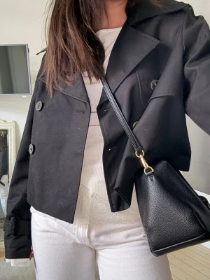 Svart kort trenchcoat  - En superfin svart trenchcoat från H&M i storlek xs. Den är anvönd 2 gånger, så i princip som ny. 