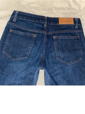 Blå utsvängda jeans från Acne - Säljer ett par blå jeans från Acne med utsvängda ben och klassisk femficksmodell. Jeansen har en snygg mörk tvätt och detaljer i kontrastsömmar.