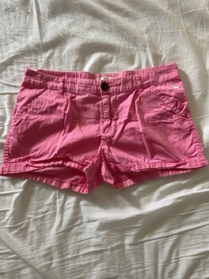 Rosa shorts från H&M - Snygga rosa shorts från H&M med klassisk knappstängning och fickor fram. Perfekta för varma dagar och har en avslappnad passform. Tillverkade i mjuk bomull som känns skön mot huden. Stilsäkert val för sommaren!