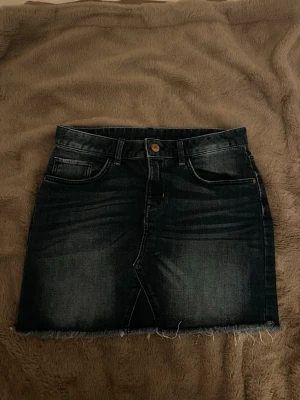 Lågmidjad jeanskjol  - Säljer en blå, kort jeanskjol som är lågmidjad, och har fransar i kanten. Storlek XS/S