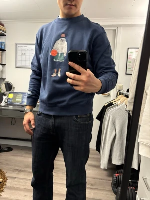 Mörkblå sweatshirt från New Balance - Mörkblå sweatshirt från New Balance med tryck av en person med basketboll på bröstet. Tröjan har rund hals, ribbade muddar och en liten NB-logga på ena ärmen. Perfekt för en avslappnad streetwear-look.