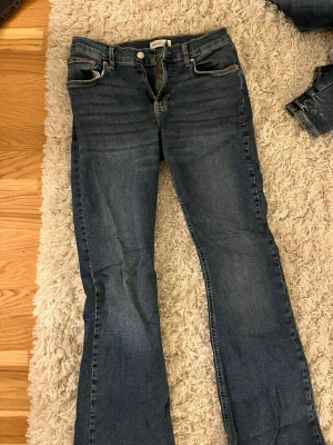 Blå bootcut jeans från Gina - Säljer ett par klassiska blå bootcut jeans från Gina med fem fickor och normalhög midja. Jeansen är tillverkade i ett mjukt denimtyg som sitter skönt. 