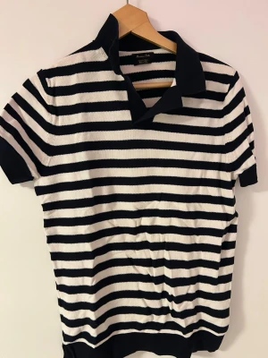 Randig kortärmad skjorta med krage - Snygg kortärmad skjorta med marinblå och vita horisontella ränder och klassisk krage. Skjortan har en relaxed fit och är tillverkad i ett mjukt stickat material som känns bekvämt mot huden. Perfekt för en avslappnad och stilren look.