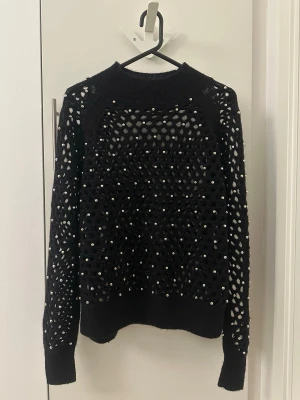 Other Stories svart tröja, storlek M - Snygg svart stickad tröja med hålmönster och små pärlor över hela plagget. Tröjan har rund halsringning, långa ärmar och ribbade muddar. Perfekt för dig som vill ha något unikt och trendigt i garderoben.