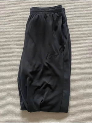 Nike träningsset  - Säljer ett träningsset från Nike som inte kommit till användning, ett par byxor med dragkedjefickor och en långärmad tröja med halv zip dragkedja. Båda plaggen har Nike-logga och är tillverkade i ett stretchigt funktionsmaterial som passar perfekt till träning. Storlek S