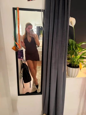 Brun prickig klänning - Kort brun klänning med små röda prickar och djup v-ringning. Klänningen är ärmlös och har en volangkant nedtill för en extra feminin touch. Perfekt för sommarens alla tillfällen. Storlek XL men sitter bra på mig som M. Aldrig använd men har ingen lapp kvar 