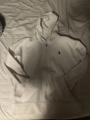 Vit zip up från Ralph lauren - En vit zip hoodie från Ralph lauren. Använd 3-5 gånger säljer pågrund av att jag inte använder den. En liten fläck på armen som är från en whiteboard penna men annars som ny, sista bilden. Pris inte hugget i sten🪨✅