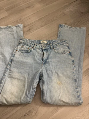 Ljusblå raka Levi's jeans - Säljer ett par klassiska ljusblå Levi's jeans med rak passform och fem fickor. Jeansen har en vintagekänsla med slitningar och en patch bak i midjan. Perfekta för en avslappnad och trendig look.