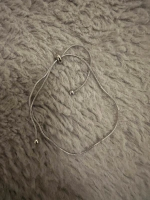 Silvrigt justerbart armband - Snyggt silvrigt armban med minimalistisk design. Armbandet har en tunn kedja och små kulor som detaljer samt ett justerbart lås för perfekt passform. Passar perfekt till dig som gillar stilrena accessoarer.