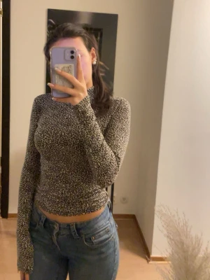 Leopardmönstrad långärmad topp från ginatricot  - Säljer en tajt och tunn långärmad topp med leopardmönster i svart och beige. Tröjan har rund halsringning och är gjord i ett stretchigt material som sitter snyggt på kroppen. 