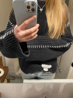 Svart stickad tröja med vita detaljer - INTRESSEKOLL!! Säljer en svart stickad tröja med vita dekorativa sömmar längs ärmarna och en vit broderad detalj nedtill. Tröjan har en avslappnad passform, långa ärmar och grovstickad struktur.  Den är i storlek cs men sitter som en S