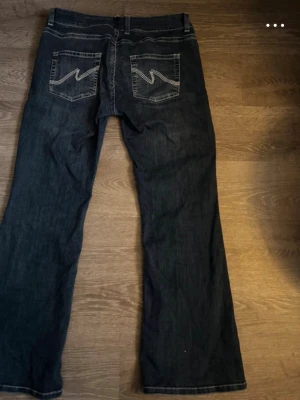 Nelly stitch jeans  - Säljer ett par mörkblå bootcut jeans med snygga broderade detaljer på bakfickorna. Jeansen har låg midja. Dom har varit insydda därav är hällan flyttad lite men inget av det insydda syns då det är uppsprättat igen! 